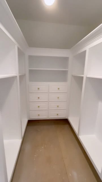 Walk-in closet with white built-in drawers and open shelves. The floor is still unfinished.